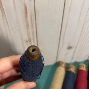 Peut inclure: Quatre bobines de fil, chacune avec une base en bois et un anneau m&eacute;tallique. Les bobines sont envelopp&eacute;es de fils de diff&eacute;rentes couleurs&nbsp;: beige, bleu marine et rouge.