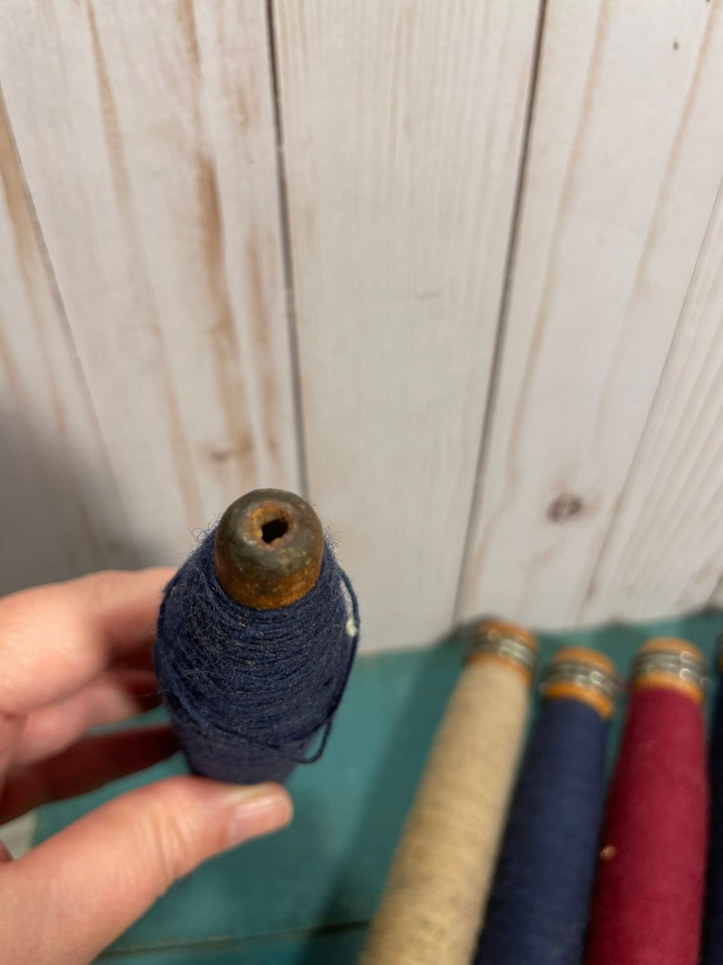 Peut inclure: Quatre bobines de fil, chacune avec une base en bois et un anneau m&eacute;tallique. Les bobines sont envelopp&eacute;es de fils de diff&eacute;rentes couleurs&nbsp;: beige, bleu marine et rouge.
