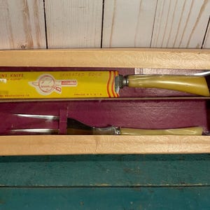 May include: A vintage Burns Knife set in its original box. The set includes a serrated edge knife and a fork with yellow plastic handles. The box is made of cardboard and has a red and yellow design.