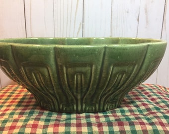 May include: A large, green ceramic bowl with a scalloped rim and a textured, geometric design. The bowl is sitting on a red and white checkered tablecloth.