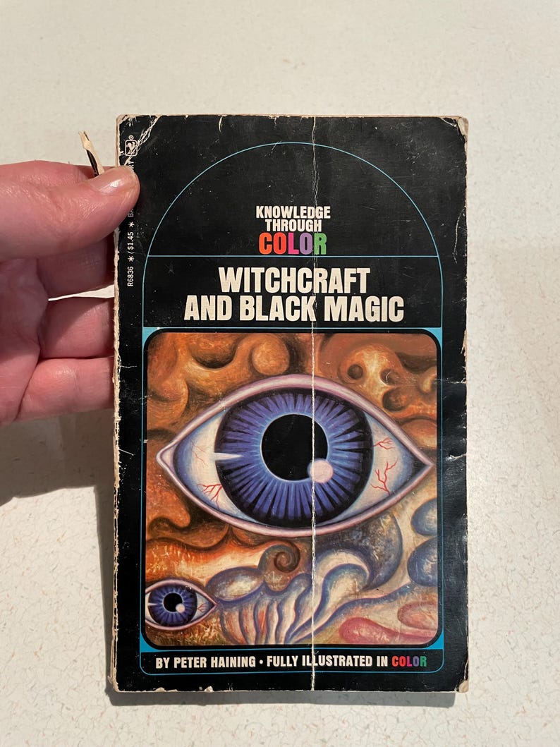 K&ouml;nnte beinhalten: Vintage Taschenbuch mit dem Titel "Witchcraft and Black Magic". Das Cover zeigt ein gro&szlig;es Auge mit blauer Iris und ein kleineres Auge darunter. Der Buchtitel ist wei&szlig;, mit "Knowledge Through Color" dar&uuml;ber.