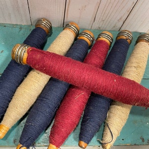 Peut inclure: Une collection de six bobines de fil vintage en bois, chacune avec un capuchon en m&eacute;tal. Les bobines sont envelopp&eacute;es de fils de diff&eacute;rentes couleurs, notamment bleu marine, rouge et beige.