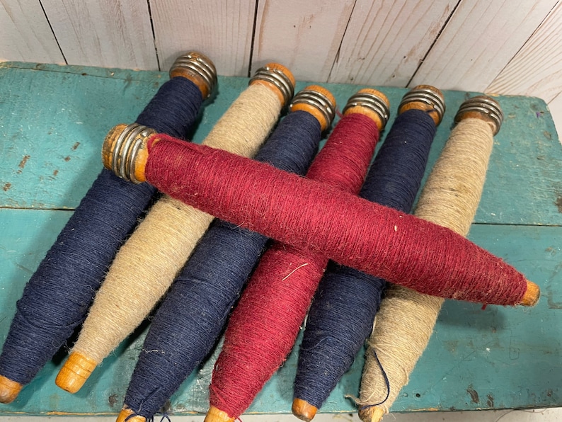 Peut inclure: Une collection de six bobines de fil vintage en bois, chacune avec un capuchon en m&eacute;tal. Les bobines sont envelopp&eacute;es de fils de diff&eacute;rentes couleurs, notamment bleu marine, rouge et beige.