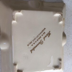 May include: A white ceramic ashtray with a gold inscription that reads "Hand Decorated 22 K Gold U.S.A.  Weeeping-Bright Gold".
