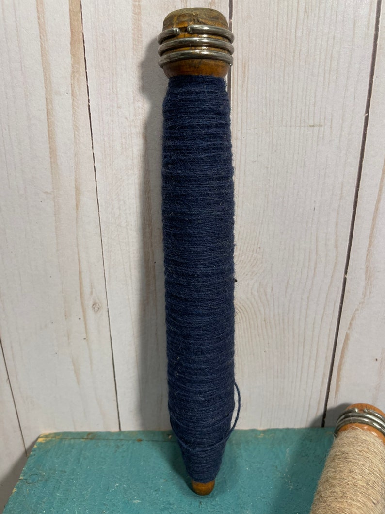 Peut inclure: Une bobine en bois avec un dessus en m&eacute;tal et une grande quantit&eacute; de fil bleu fonc&eacute; enroul&eacute; autour.