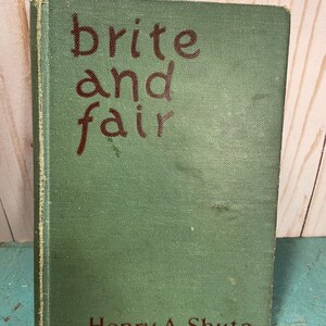 Puede incluir: Un libro antiguo titulado "brite and fair" de Henry A. Shute. El libro tiene una cubierta verde con el título y el nombre del autor en rojo oscuro. La cubierta del libro muestra signos de desgaste.