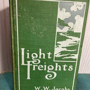 May include: A vintage book titled "Light Freights" by W.W. Jacobs. The cover is green with white lettering and a rectangular illustration of a river scene with a boat. The book is in good condition.