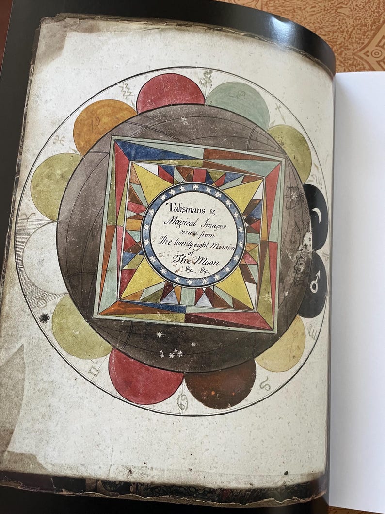 K&ouml;nnte beinhalten: Offene Buchseite mit einer detaillierten Illustration eines kreisf&ouml;rmigen Diagramms mit farbenfrohen geometrischen Formen, astrologischen Symbolen und Text. Das zentrale Design ist ein Quadrat in einem Kreis, mit dem Text "Talismans & Magical Images".