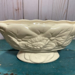 May include: A white ceramic bowl with a floral design. The bowl has a pedestal base and is ideal for serving or displaying flowers.