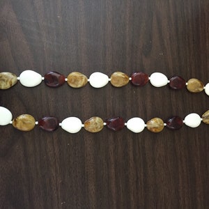 Könnte beinhalten: Eine lange Halskette aus braunen, weißen und bernsteinfarbenen ovalen Perlen.