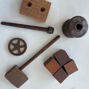 May include: A collection of vintage wooden tools and objects, including a mallet, a wooden dowel, a small wooden wheel, a wooden block with holes, and a brown ceramic spool.