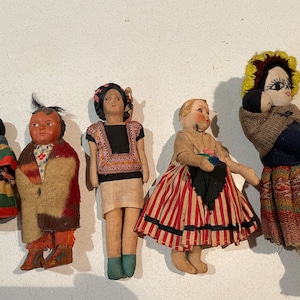 Könnte beinhalten: Fünf antike Stoffpuppen mit unterschiedlichen Ethnien und Kleidungsstilen. Die Puppen sind handgefertigt und haben bemalte Gesichter. Sie tragen bunte Kleidung und Accessoires.