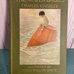 May include: Vintage hardcover book titled "The Water-Babies" by Charles Kingsley, illustrated by Jessie Willcox Smith. The cover is olive green with gold lettering. The illustration depicts a child sitting on a buoy in the water.