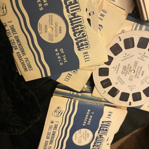 May include: A close-up of a stack of View-Master reels. The reels are labelled with the text "View-Master Reel" and "7 More Wonders". The reels are for three-dimensional pictures in full colour Kodachrome. The reels are from the 1950s and 1960s.