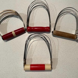 Könnte beinhalten: Drei antike Teigroller mit roten und weißen Griffen. Die Teigroller sind aus Metall und haben ein Drahtdesign.