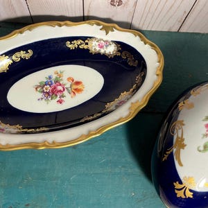 May include: An oval, navy blue and white porcelain dish and an egg-shaped container. Both pieces feature gold trim and floral designs. The dish measures approximately 10 inches long.