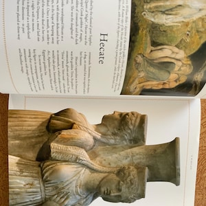 K&ouml;nnte beinhalten: Ein Foto einer Buchseite mit einer Skulptur der griechischen G&ouml;ttin Hekate. Die Skulptur, in hellem Beige, zeigt drei Figuren. Das Wort "Hekate" ist auf der Seite zu sehen.
