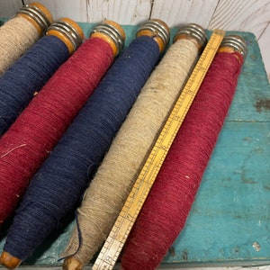 Peut inclure: Cinq bobines de fil en bois, chacune avec une bande m&eacute;tallique autour du centre. Les bobines sont envelopp&eacute;es de fils de diff&eacute;rentes couleurs&nbsp;: rouge, bleu, beige et rouge. Une r&egrave;gle en bois est pos&eacute;e sur les bobines.