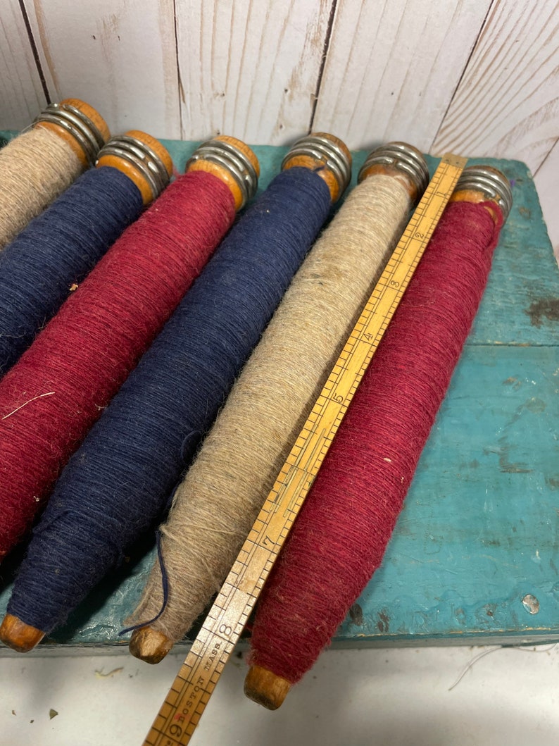 Peut inclure: Cinq bobines de fil en bois, chacune avec une bande m&eacute;tallique autour du centre. Les bobines sont envelopp&eacute;es de fils de diff&eacute;rentes couleurs&nbsp;: rouge, bleu, beige et rouge. Une r&egrave;gle en bois est pos&eacute;e sur les bobines.