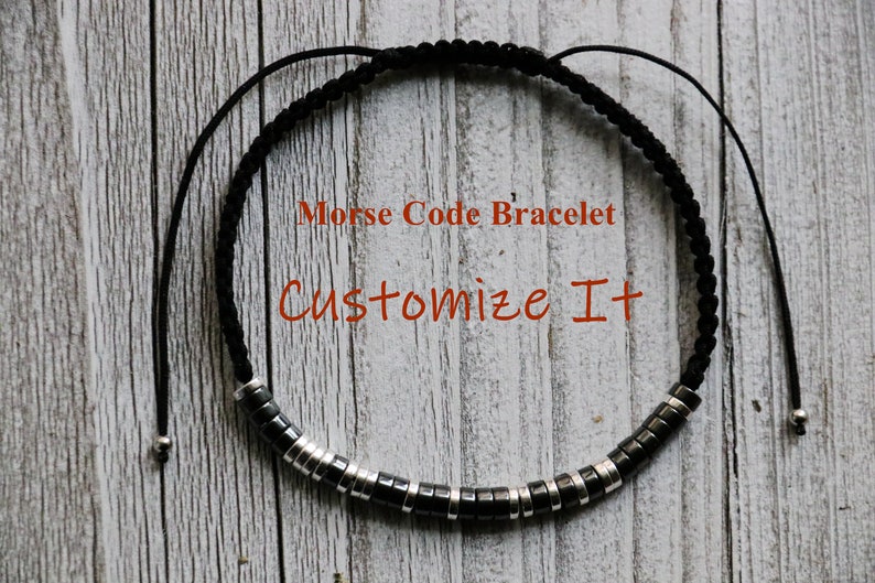 May include: A black cord bracelet with silver beads that spell out a message in Morse code. The bracelet is adjustable and has a sliding knot. The text on the image reads "Morse Code Bracelet Customize It".