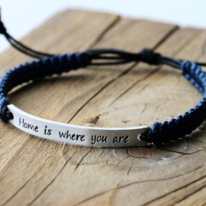 May include: A blue and black braided bracelet with a silver charm that reads "Home is where you are".