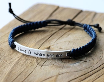 May include: A blue and black braided bracelet with a silver charm that reads "Home is where you are".