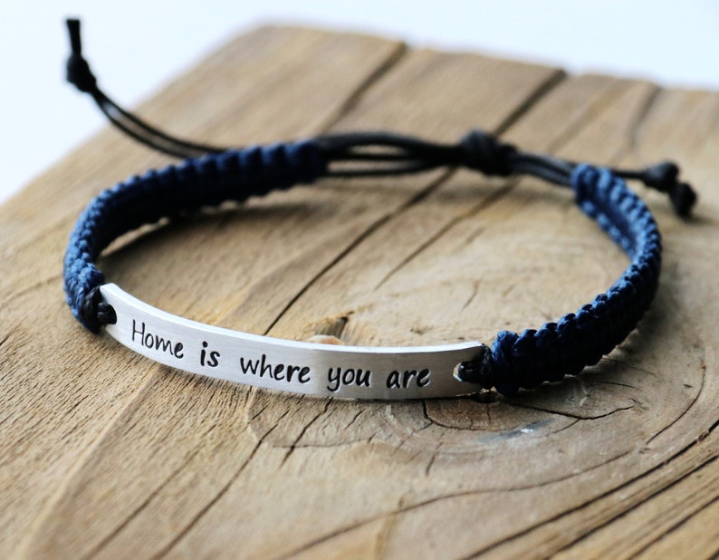 May include: A blue and black braided bracelet with a silver charm that reads "Home is where you are".