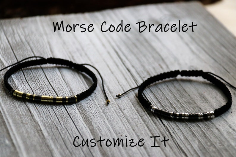 May include: Two black cord bracelets with gold and silver beads. The bracelets are on a wooden surface. The text "Morse Code Bracelet" and "Customize It" are visible.