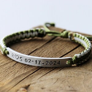 May include: A green and white braided bracelet with a silver bar charm engraved with "R&hearts;S 02-17-2024".