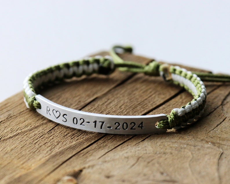 May include: A green and white braided bracelet with a silver bar charm engraved with "R&hearts;S 02-17-2024".