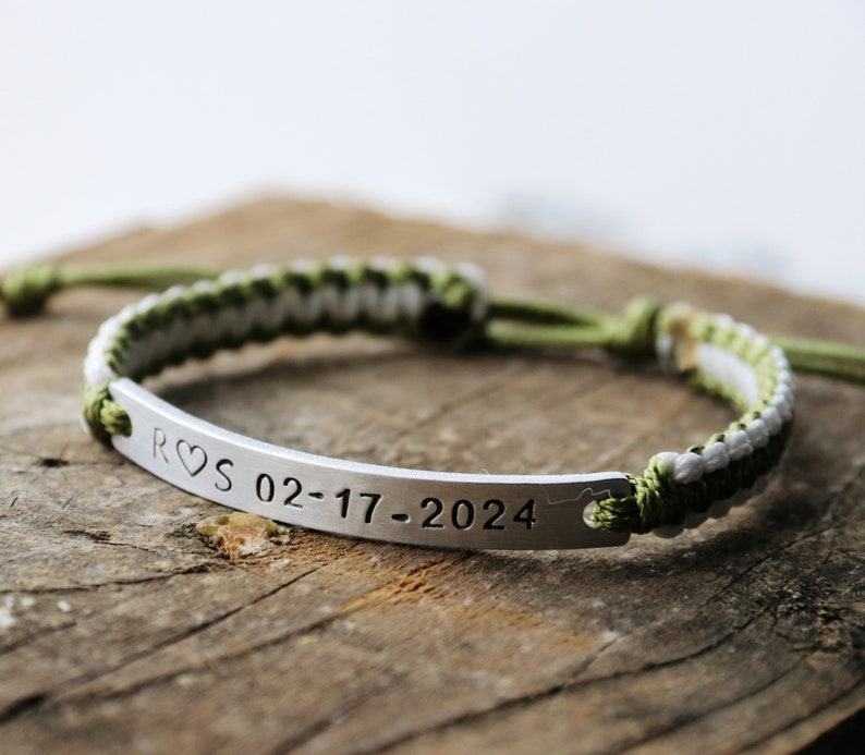 May include: A green and white braided cord bracelet with a silver metal bar engraved with "R&hearts;S 02-17-2024".