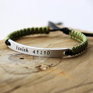May include: A green and black braided bracelet with a silver bar that says "Isaiah 41:10".