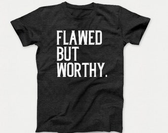 May include: A dark grey t-shirt with the text "Flawed But Worthy." printed in white.