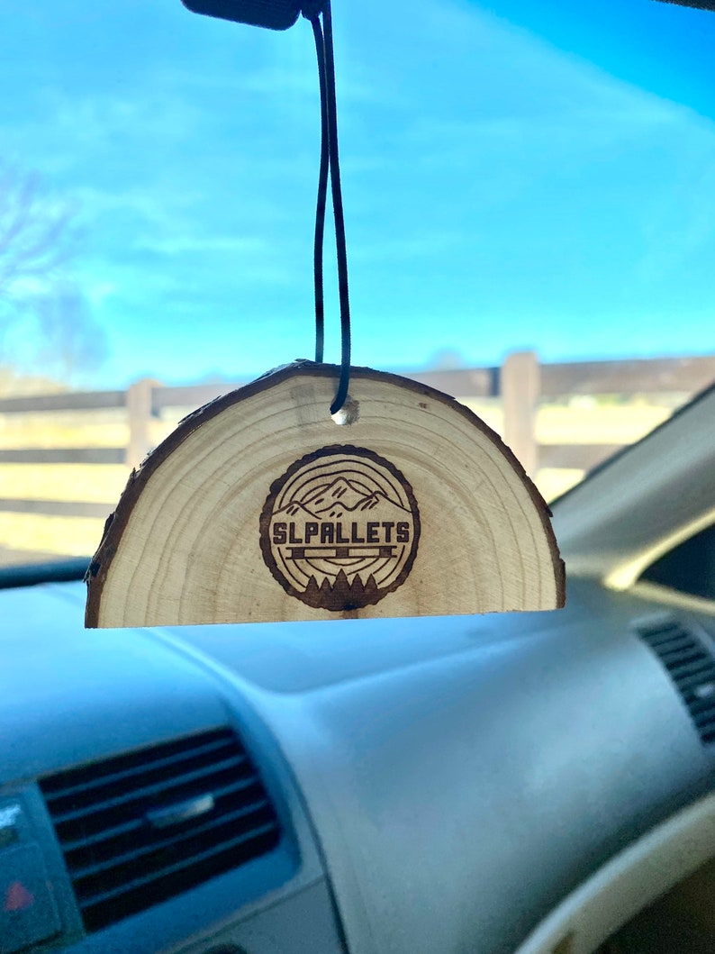 Peut inclure: Un diffuseur d'air de voiture en bois avec une finition en bois brun. Le diffuseur d'air a la forme d'un demi-cercle et est dot&eacute; d'une ficelle noire pour l'accrocher. Le diffuseur d'air pr&eacute;sente un motif de montagnes et d'arbres br&ucirc;l&eacute;s au bois avec le texte "SL PALLETS" au centre.