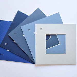 Puede incluir: Un abanico de paspart&uacute;s cuadrados de papel en varios tonos de azul, desde azul marino intenso hasta gris claro. Cada cart&oacute;n est&aacute; etiquetado con un n&uacute;mero, incluyendo 12, 13, 37, 25 y 27, con el cart&oacute;n superior presentando un recorte cuadrado.