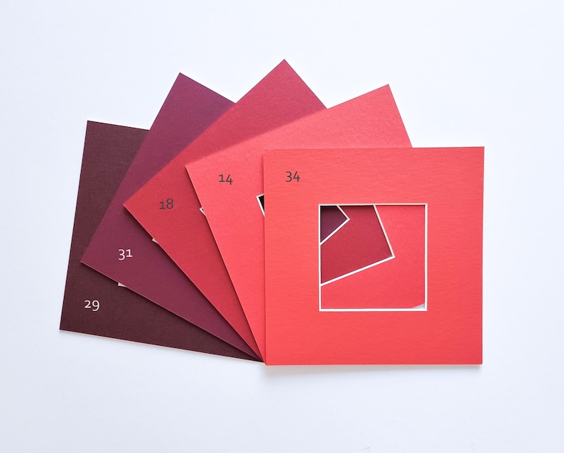 Puede incluir: Un abanico de cinco paspart&uacute;s cuadrados de papel en varios tonos de rojo, desde el burdeos intenso hasta el coral brillante. Cada paspart&uacute; presenta un recorte cuadrado central y est&aacute; etiquetado con los n&uacute;meros 29, 31, 18, 14 y 34.