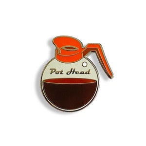 May include: A gold-colored enamel pin shaped like a coffee pot with a red lid and handle. The pot is filled with brown coffee and has the text "Pot Head" written on the side.
