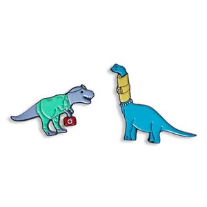 May include: Two dinosaur enamel pins. One is a T-Rex wearing a green medical uniform and holding a red first aid kit. The other is a blue Brachiosaurus with a yellow neck brace and a pearl necklace.