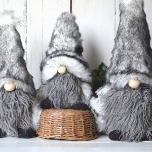 Peut inclure: Trois gnomes gris et blancs en fourrure avec de longues barbes. Le gnome du milieu est assis sur un panier tissé.