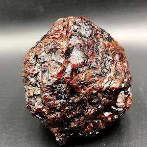 Könnte beinhalten: Ein großer, rauer, dunkelroter Edelstein mit kristalliner Struktur. Der Edelstein hat eine tiefe, satte Farbe und ist ein wunderschönes Beispiel für ein natürliches Mineral.