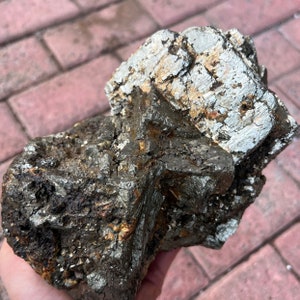 Könnte beinhalten: Ein großer, rauer, grauer und goldener Pyrit-Kristallcluster. Der Kristall hat einen metallischen Glanz und besteht aus mehreren verwachsenen Kristallen.