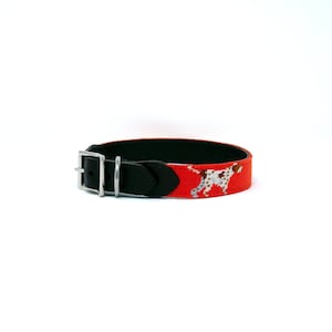 May include: Red dog collar with a black leather backing and a silver buckle. The collar features a white and brown dog illustration.