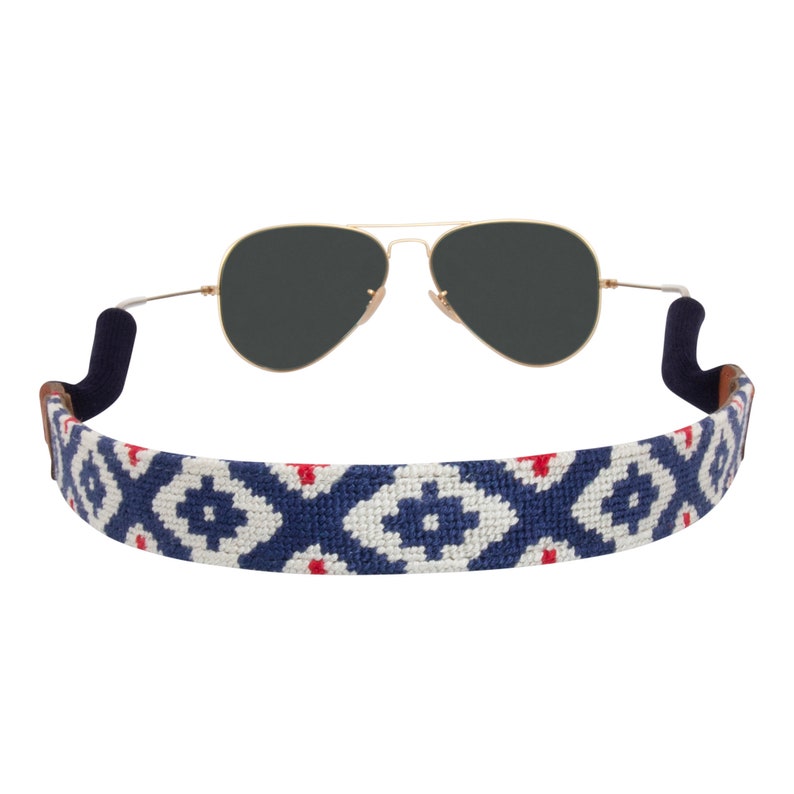 May include: A white and blue patterned sunglass strap with red accents. The strap is made of woven fabric and has a soft, comfortable feel.