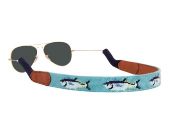 May include: A light blue sunglass strap with a brown leather accent and a repeating pattern of yellowfin tuna fish.