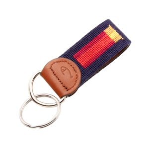 May include: A navy blue key chain with a red and yellow striped pattern. The key chain has a brown leather loop with a fish logo and two silver key rings.