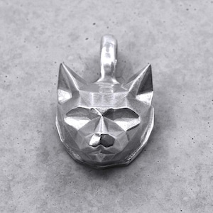 Könnte beinhalten: Ein silberner Katzenanhänger mit geometrischem, facettiertem Design. Der Anhänger zeigt einen Katzenkopf mit spitzen Ohren und einer Schlaufe für eine Kette. Der Anhänger besteht aus glänzendem Metall.