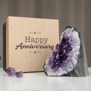 May include: A purple amethyst crystal cluster in the shape of a cave, with the words "Happy Anniversary" on a brown box behind it.