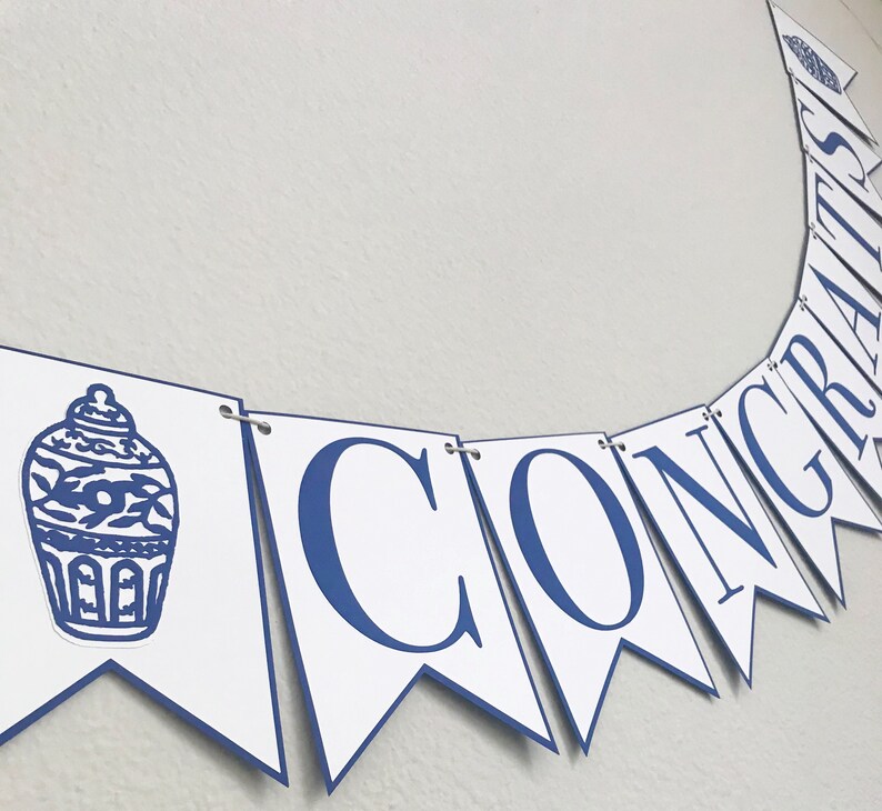 K&ouml;nnte beinhalten: Ein wei&szlig;-blaues Banner mit dem Wort "CONGRATS" in blauen Buchstaben. Das Banner hat auf der linken Seite ein blaues und wei&szlig;es chinesisches Porzellanmuster.