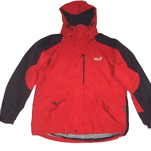 Op de afbeelding: Rode en zwarte jas met capuchon, ritssluiting en het Jack Wolfskin-logo. De jas heeft zwarte mouwen en een rode body. Het heeft een capuchon en meerdere zakken, geschikt voor buitenactiviteiten.