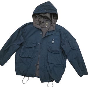 May include: A navy blue hooded jacket with multiple pockets and a drawstring hem. The jacket features a button-up front and a contrasting brown lining in the hood. A small logo is visible on the chest.